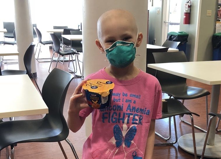 Young girl with mask holds macaroni and cheese container
