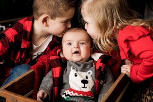 Big brother and sister giving baby brother a kiss on each cheek.