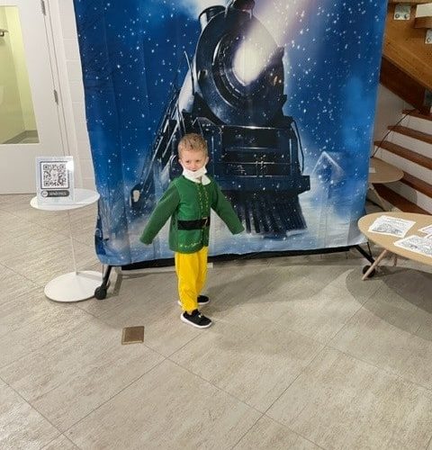 Child in elf costume standing in front of a background depicting a train