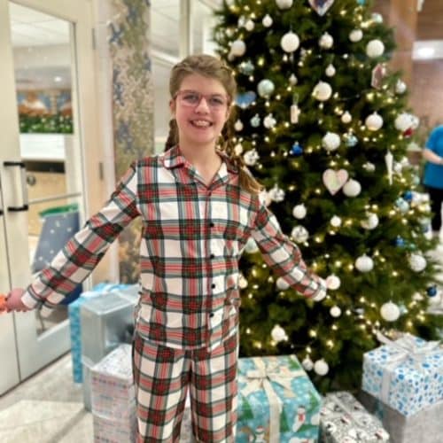 A child wearing Christmas pajamas in front of a Christmas tree