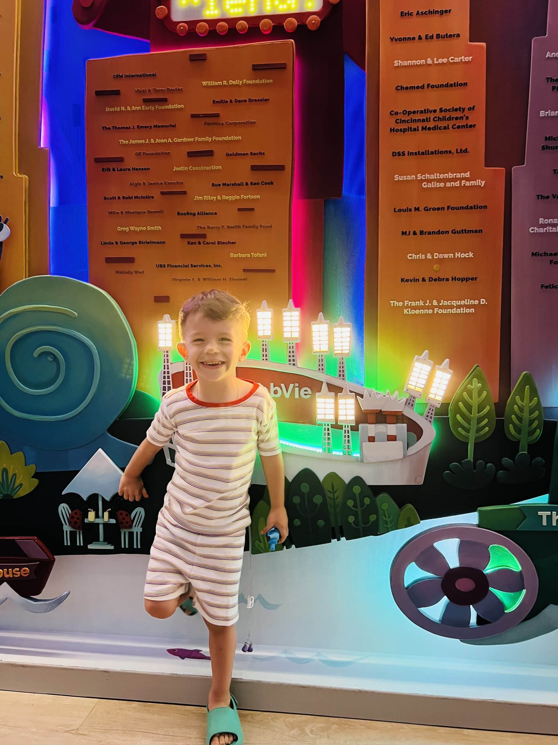 Boy smiling in front of a wall with lights behind him.