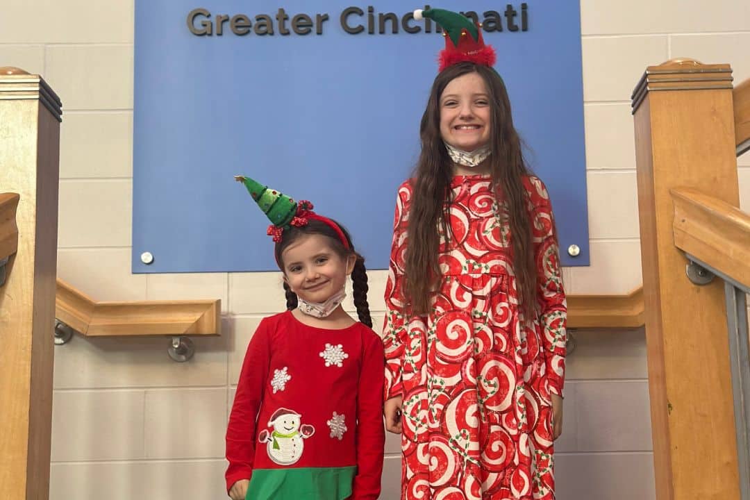 Big and little sister in holiday outfits and headbands posing for a photo.