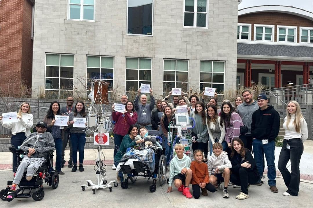 Group photo of two boys in wheelchairs and celebration signs.