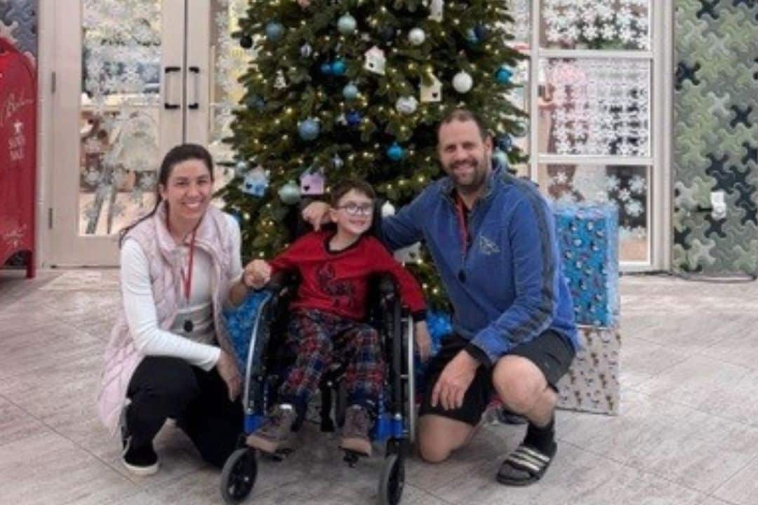 Family of three smiling in front of Christmas tree.
