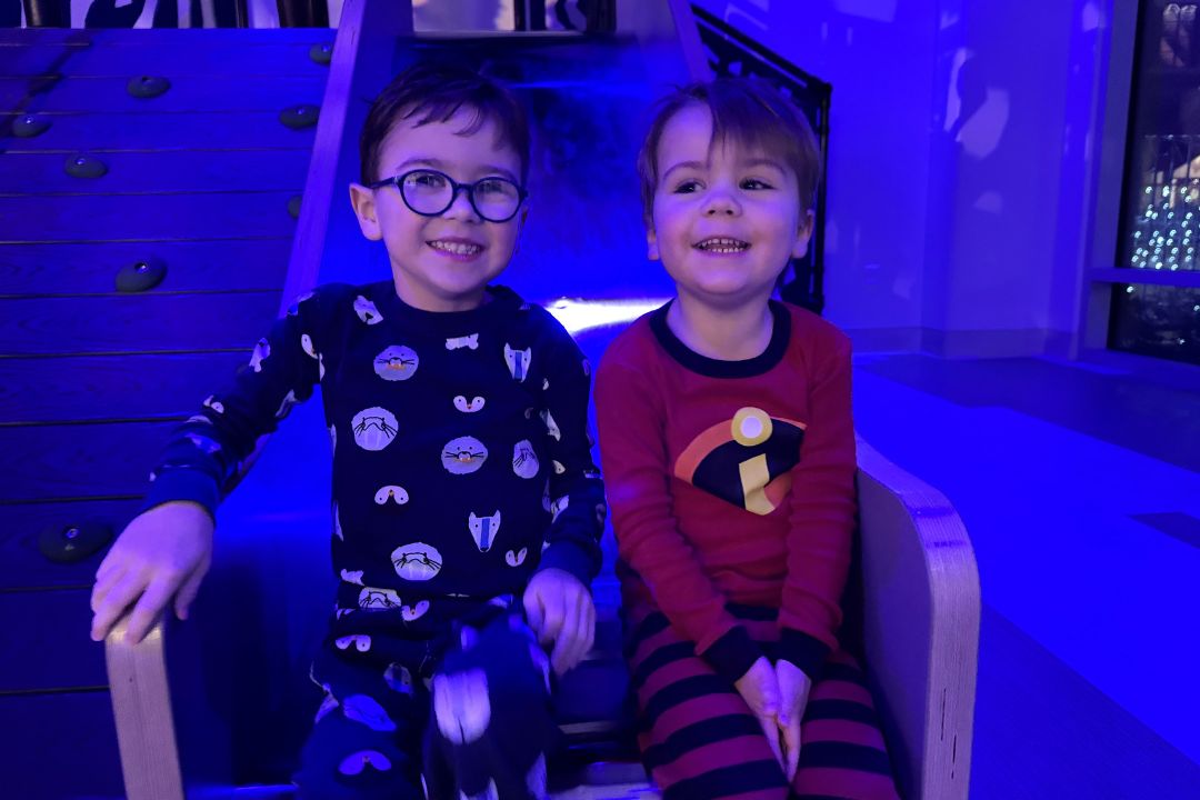 Two boys sitting at the end of the slide in a glowing room.